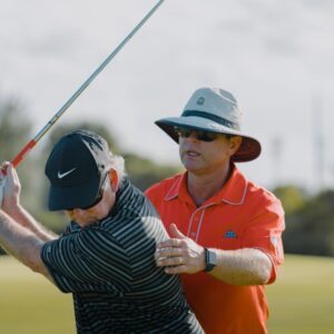 A man in an orange shirt is holding onto a golf club