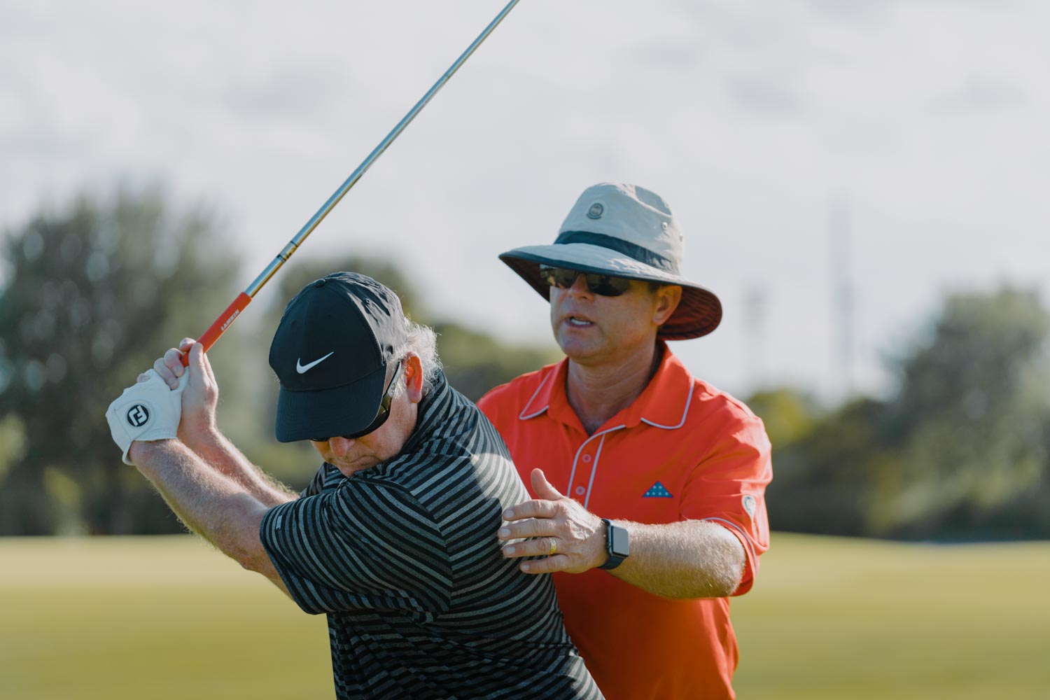 A man in an orange shirt is holding onto a golf club