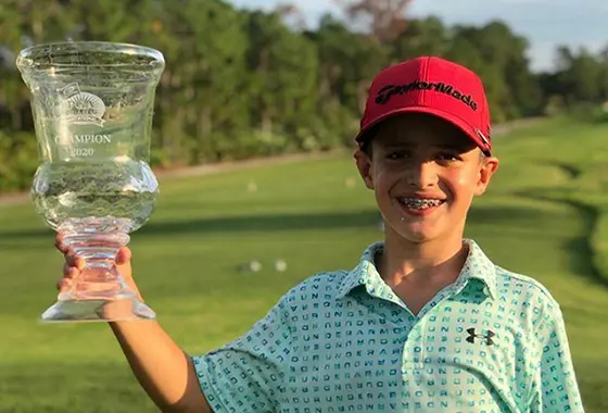 A boy holding up a glass trophy on top of a golf course.