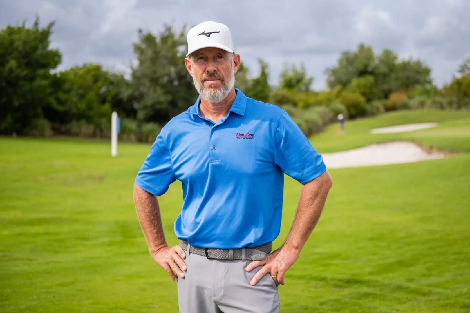 A man in blue shirt and cap standing on grass.