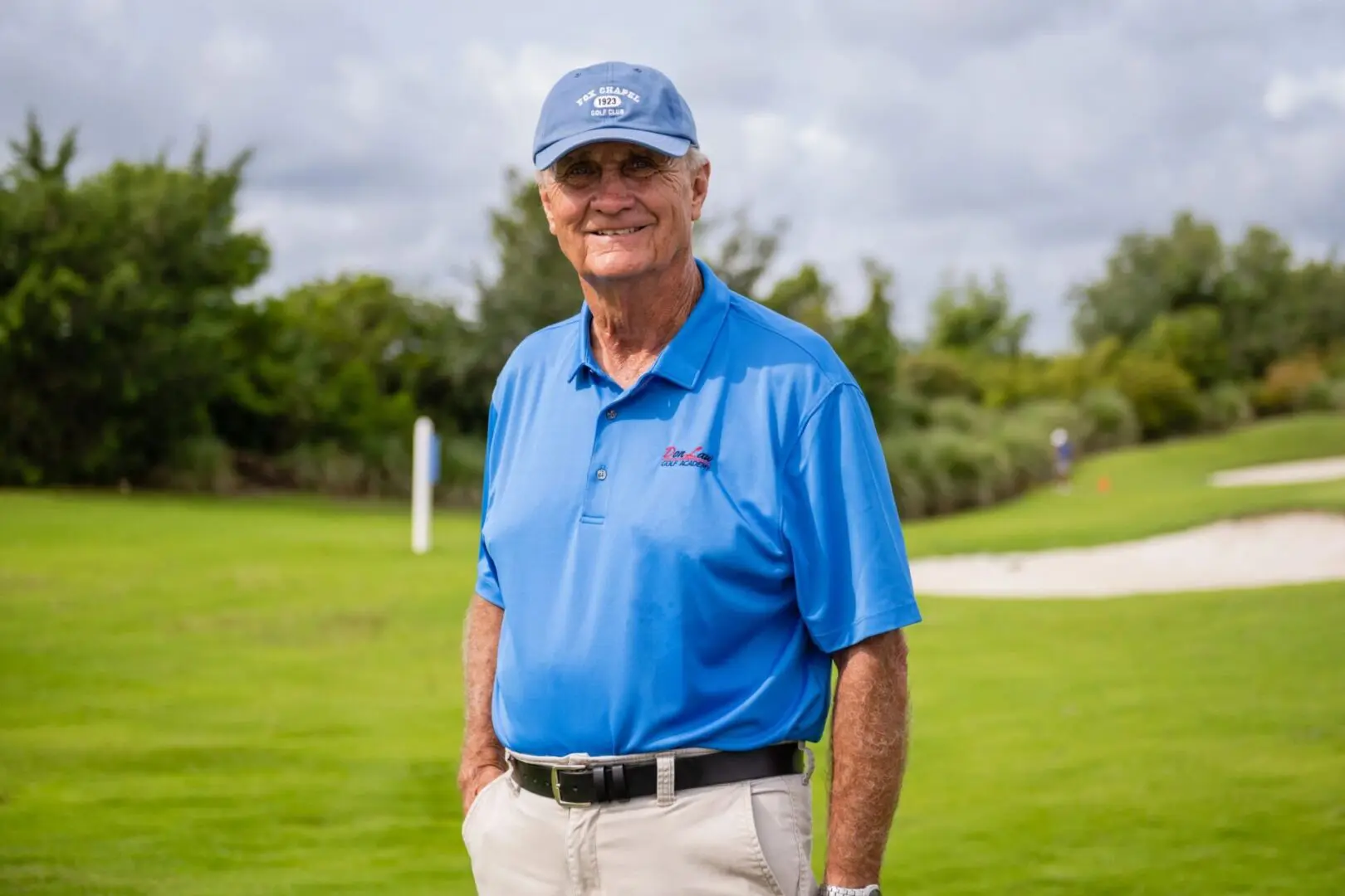 A man in blue shirt and hat standing on grass.