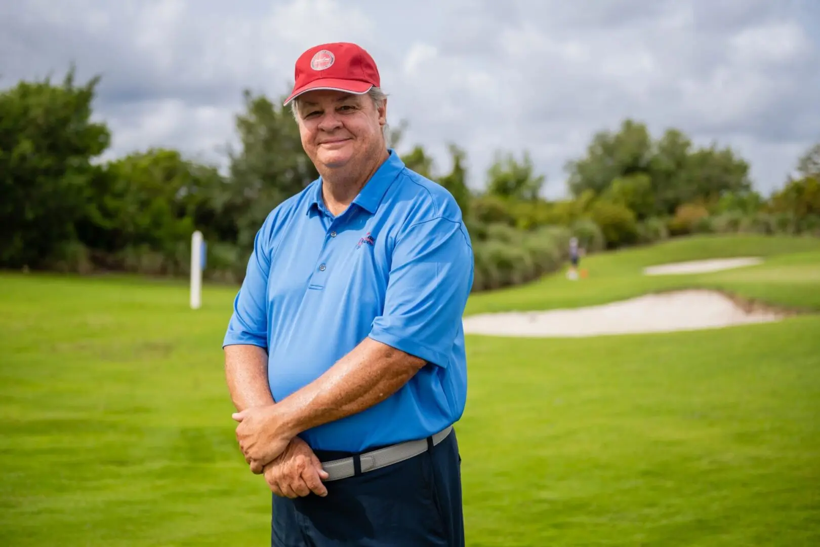 A man in blue shirt and red hat standing on grass.