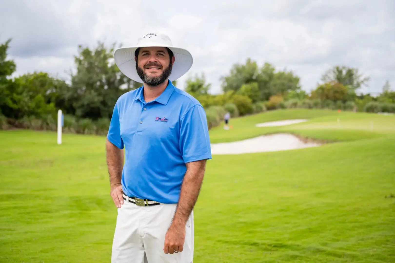 A man in blue shirt and white hat standing on grass.