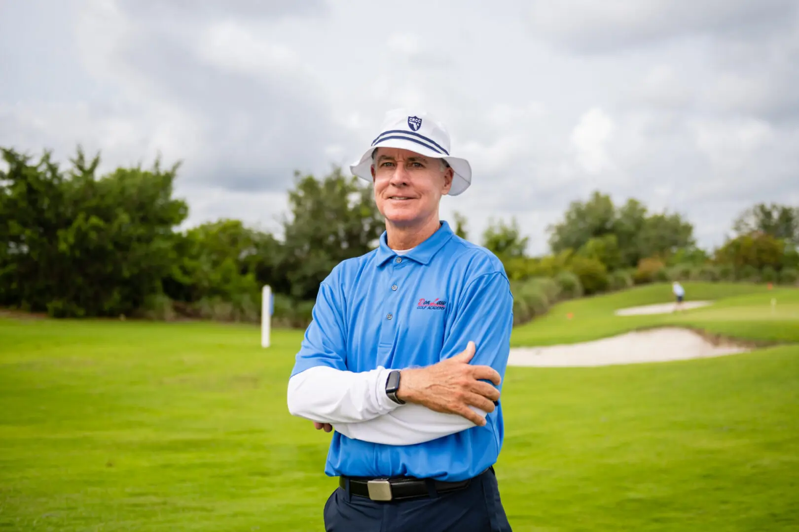 A man in blue shirt and hat standing on grass.