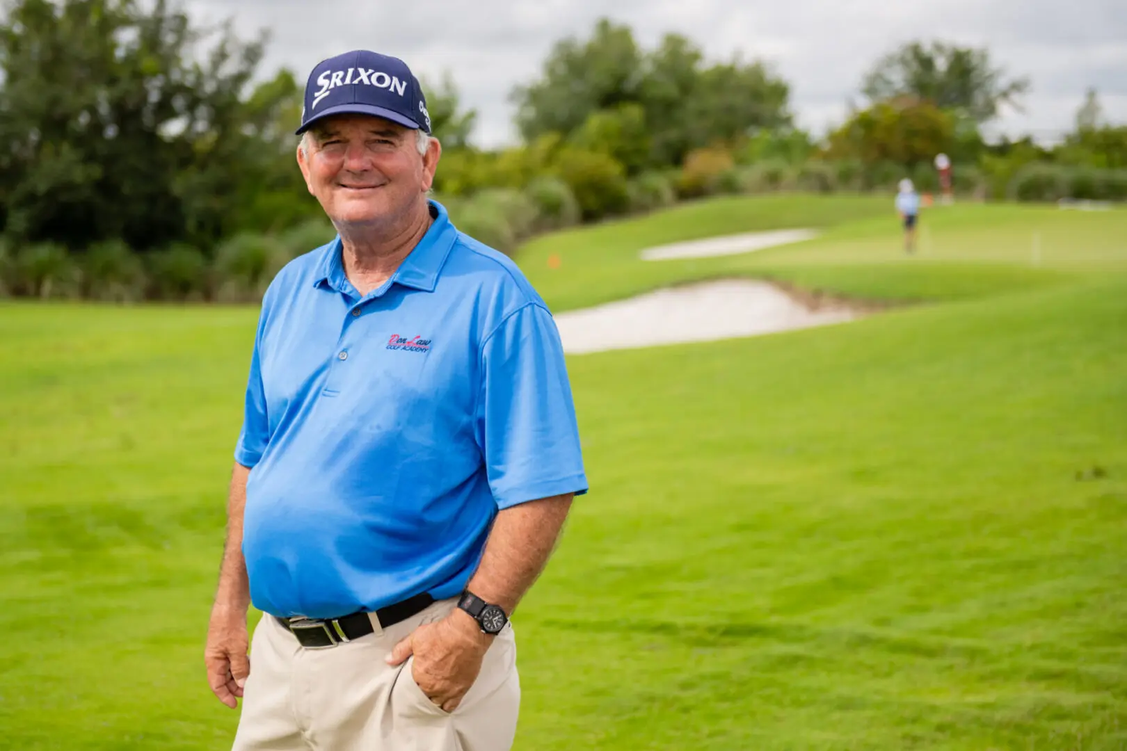 A man in blue shirt and hat standing on grass.