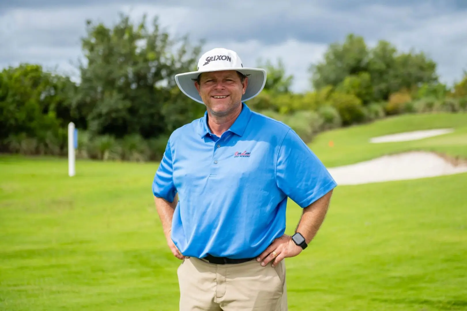 A man in blue shirt and hat standing on grass.