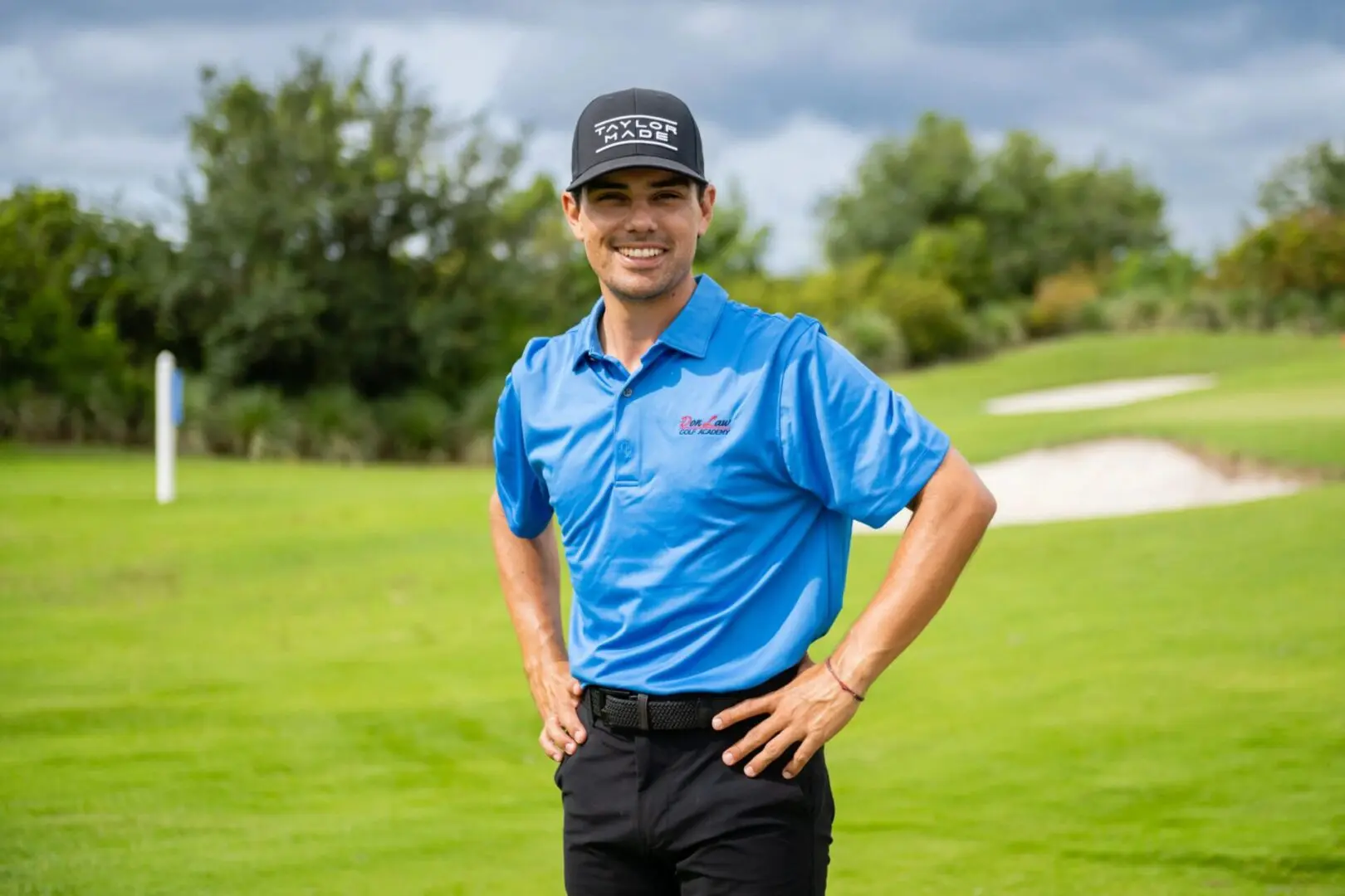 A man in blue shirt and hat standing on grass.