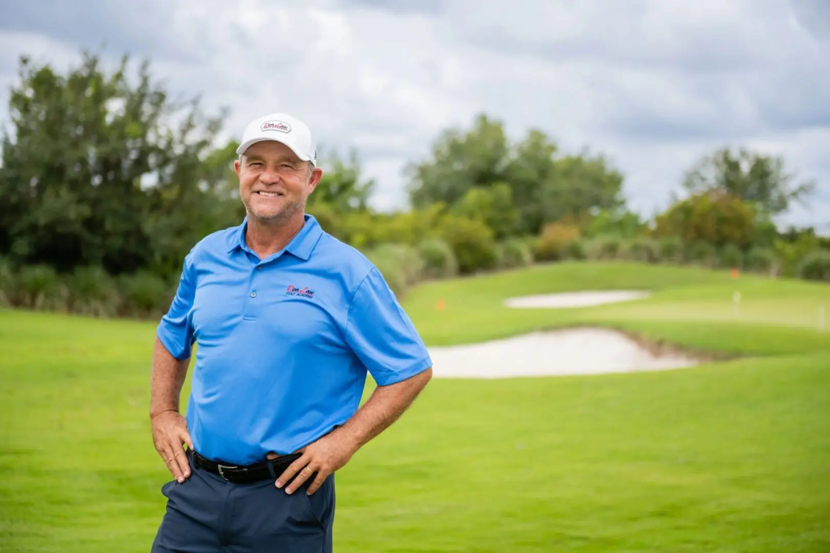 A man in blue shirt standing on grass near trees.