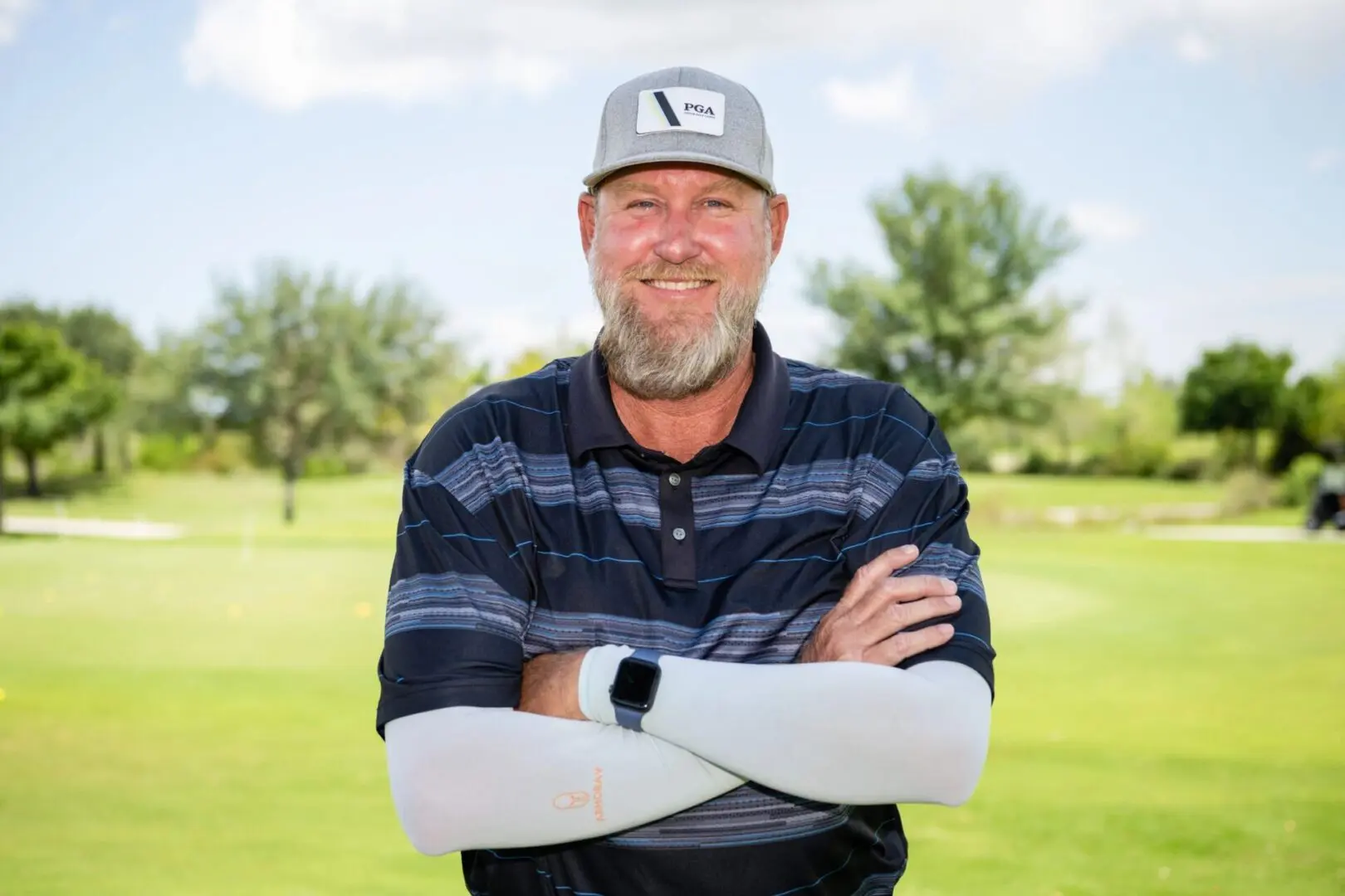 A man with his arms crossed on the golf course.