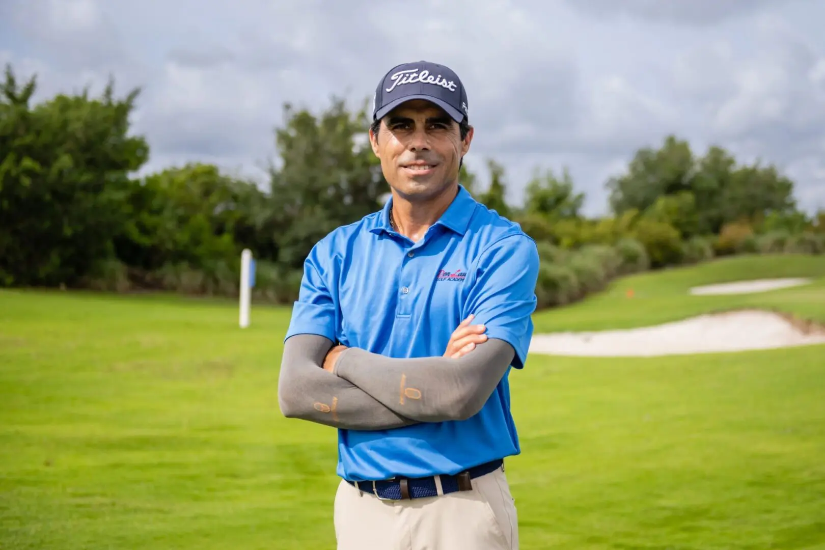 A man in blue shirt and hat standing on grass.